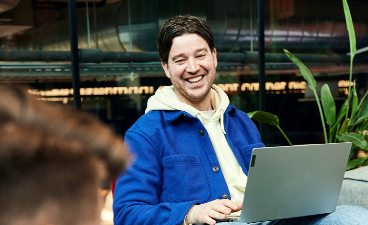 Man kijkt lachend achter laptop