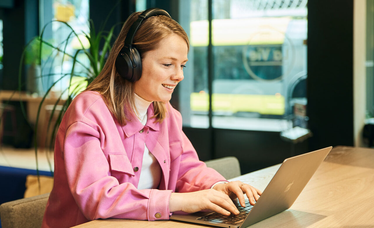 Vrouw zit met koptelefoon achter haar laptop