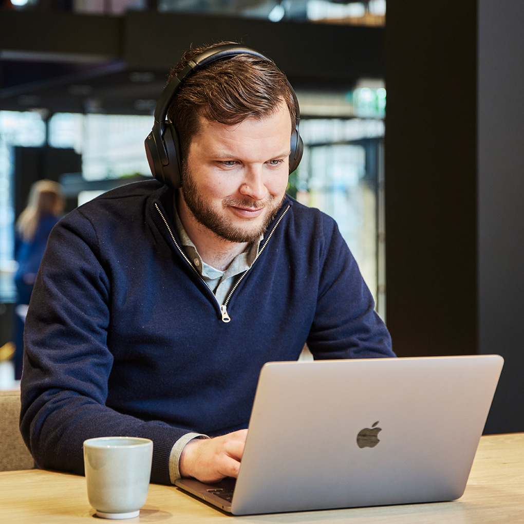 Man met koptelefoon zit achter laptop met koffie
